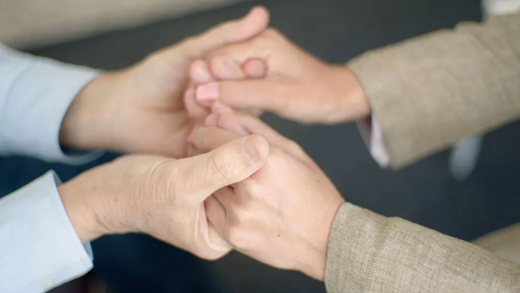 Two people clasping hands across a table in reassurance
