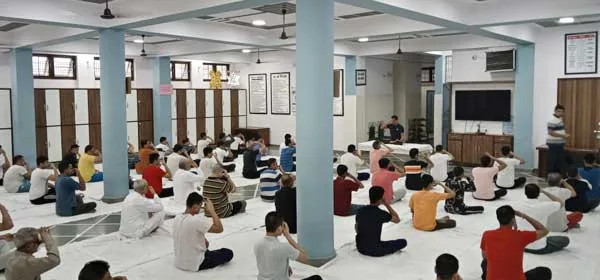 A group of people seated on the floor in a large hall during a group session