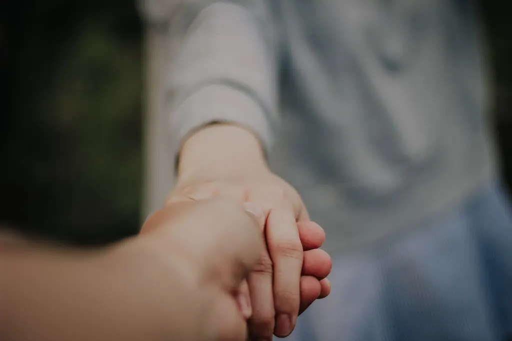 One person gently holding another person’s hand in support