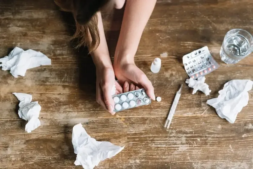 A person holding medicine strips beside crumpled tissues