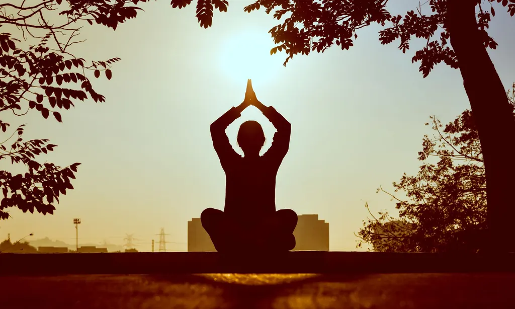 A person meditating outdoors at sunrise