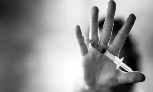 A hand raised in a stop gesture with a syringe between the fingers